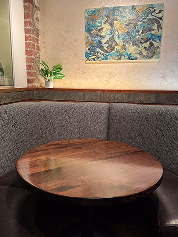Round walnut restaurant booth table set into a curved upholstered booth, with a koi-fish painting on the wall behind