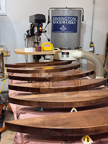 Five round dining table tops in a row drying in the workshop, with the Kensington Woodworks branded dust collector behind them