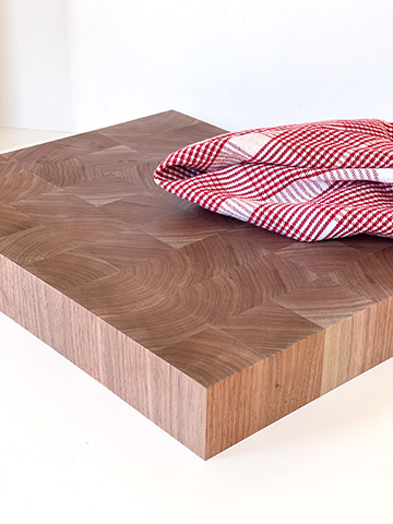 A thick walnut end-grain butcher block on a clean white surface with a red and white kitchen towel draped over one corner